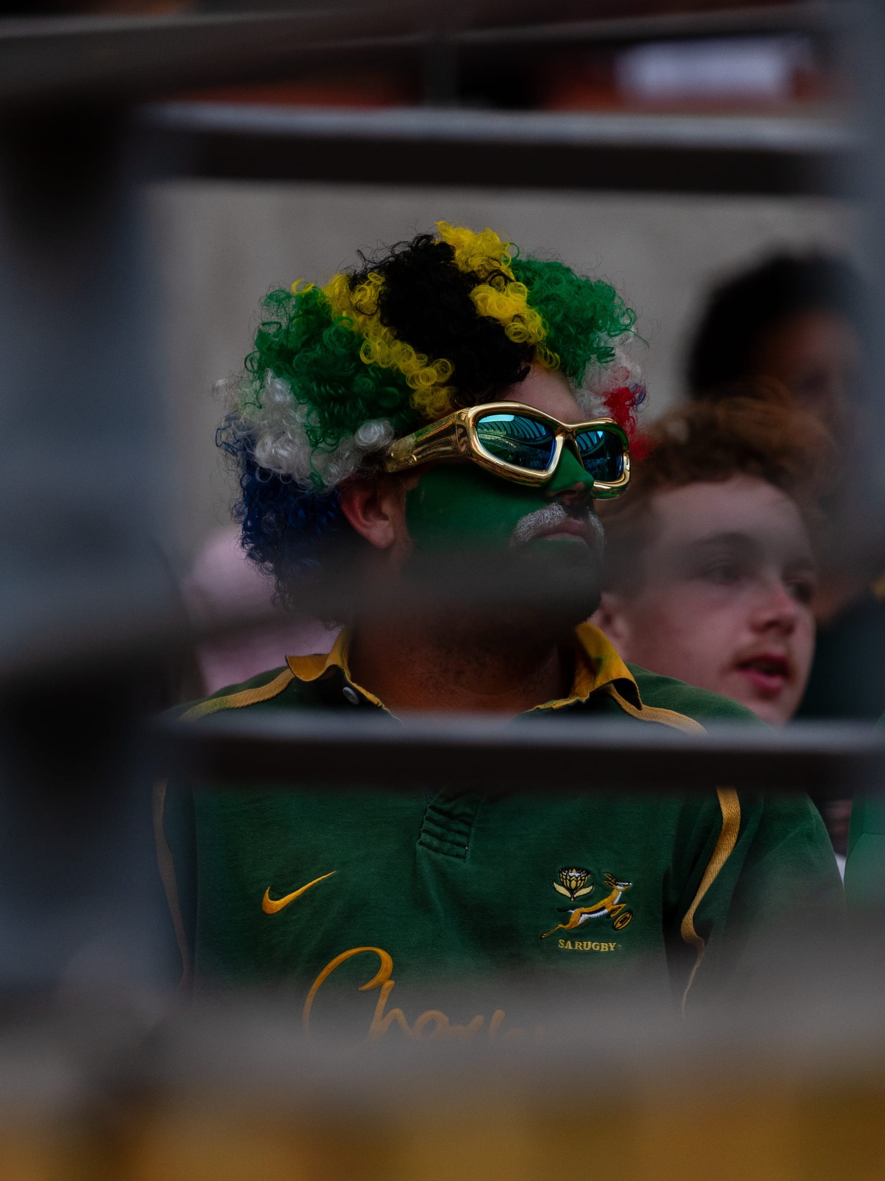 Supporter in a green and gold wig watching the match from the stands